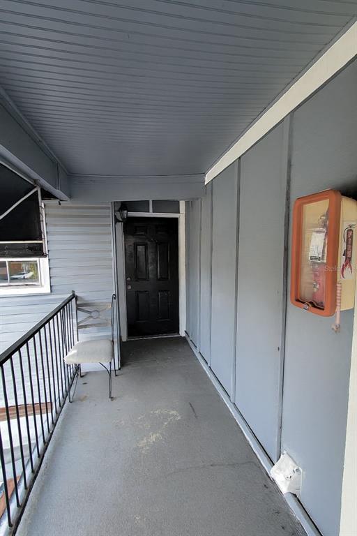 A covered outdoor walkway features a black door, a metal railing, and a wall-mounted fire extinguisher — 200 COUNTRY CLUB DR UNIT 1302, LARGO, FL