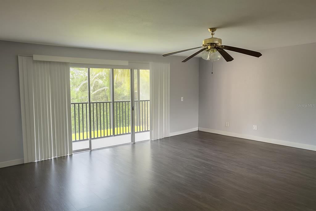 An empty living room features dark wood-look flooring, a ceiling fan, and sliding glass doors — 200 COUNTRY CLUB DR UNIT 1302, LARGO, FL