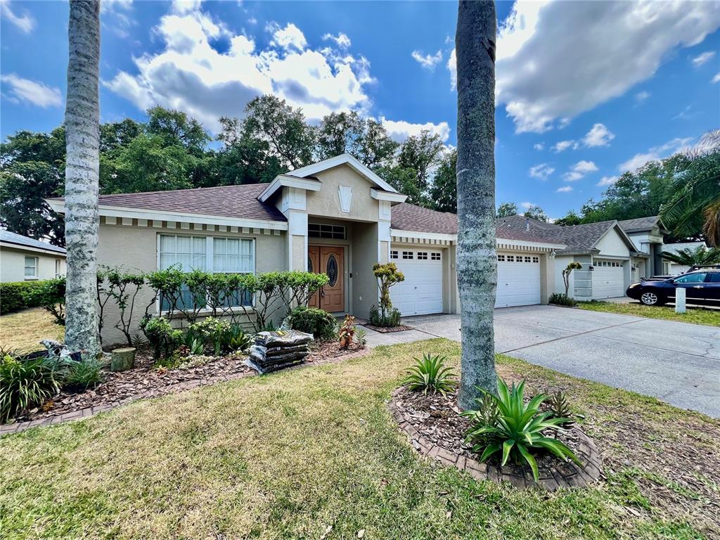 A single-story house with a beige stucco exterior, a two-car garage, and two palm trees — 18241 COLLRIDGE DRIVE, TAMPA, FL