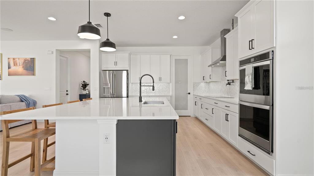 A modern kitchen features white cabinetry, a dark gray island, and stainless steel appliances — 15239 LAKE LAMONIA ST, WINTER GARDEN, FL
