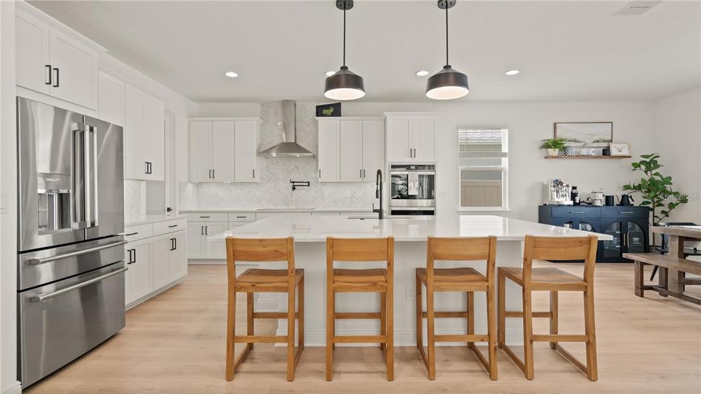 A modern kitchen features white cabinetry, a large central island with wooden stools, and stainless appliances — 15239 LAKE LAMONIA ST, WINTER GARDEN, FL