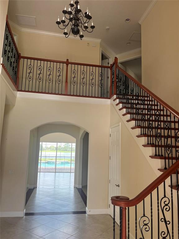 A foyer features a staircase with iron railings, a chandelier, and an arched entryway — 18229 BELLEZZA DRIVE, ORLANDO, FL