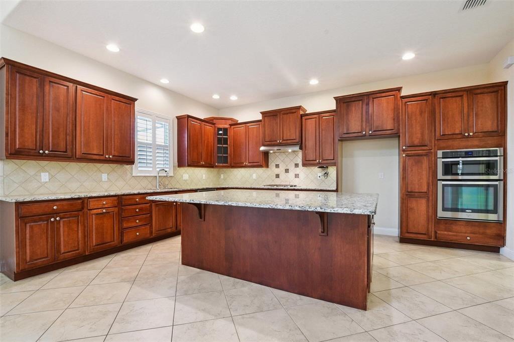 A kitchen with cherry wood cabinets, granite countertops, a large island, and tile flooring — 18229 BELLEZZA DRIVE, ORLANDO, FL