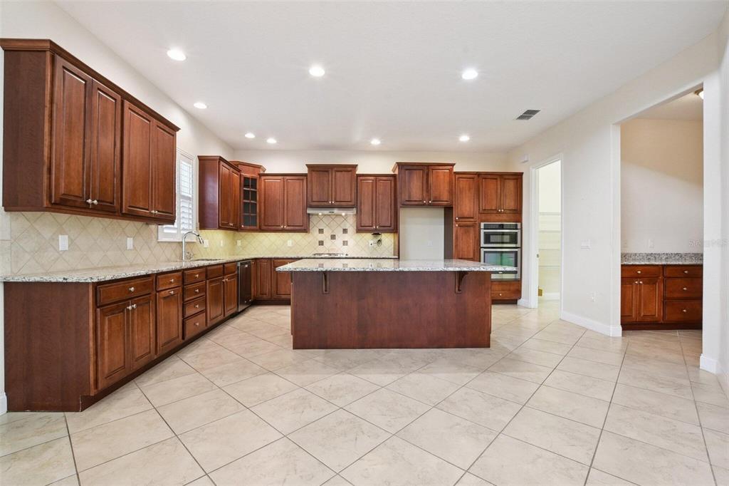 A kitchen with dark wood cabinets, granite countertops, a central island, and tile flooring — 18229 BELLEZZA DRIVE, ORLANDO, FL