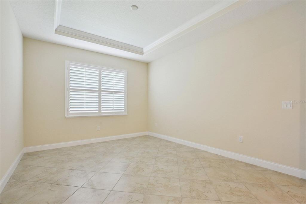 An empty room with beige walls, tile flooring, and a window with white plantation shutters — 18229 BELLEZZA DRIVE, ORLANDO, FL
