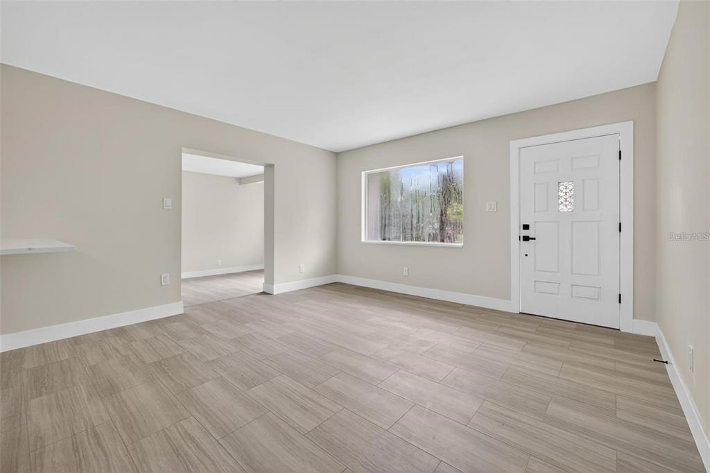 A bright living room features light wood-look tile flooring, neutral walls, and a white front door — 413 COUNTRY CLUB DRIVE, OLDSMAR, FL