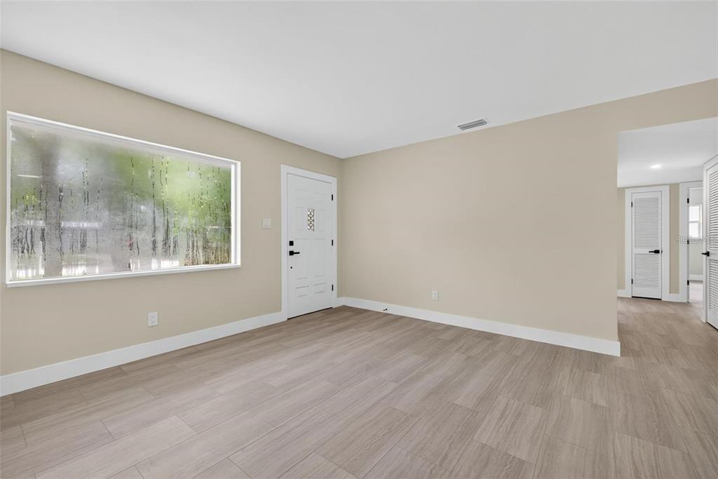 An empty room features light wood-look flooring, beige walls, a large window, and a white door — 413 COUNTRY CLUB DRIVE, OLDSMAR, FL
