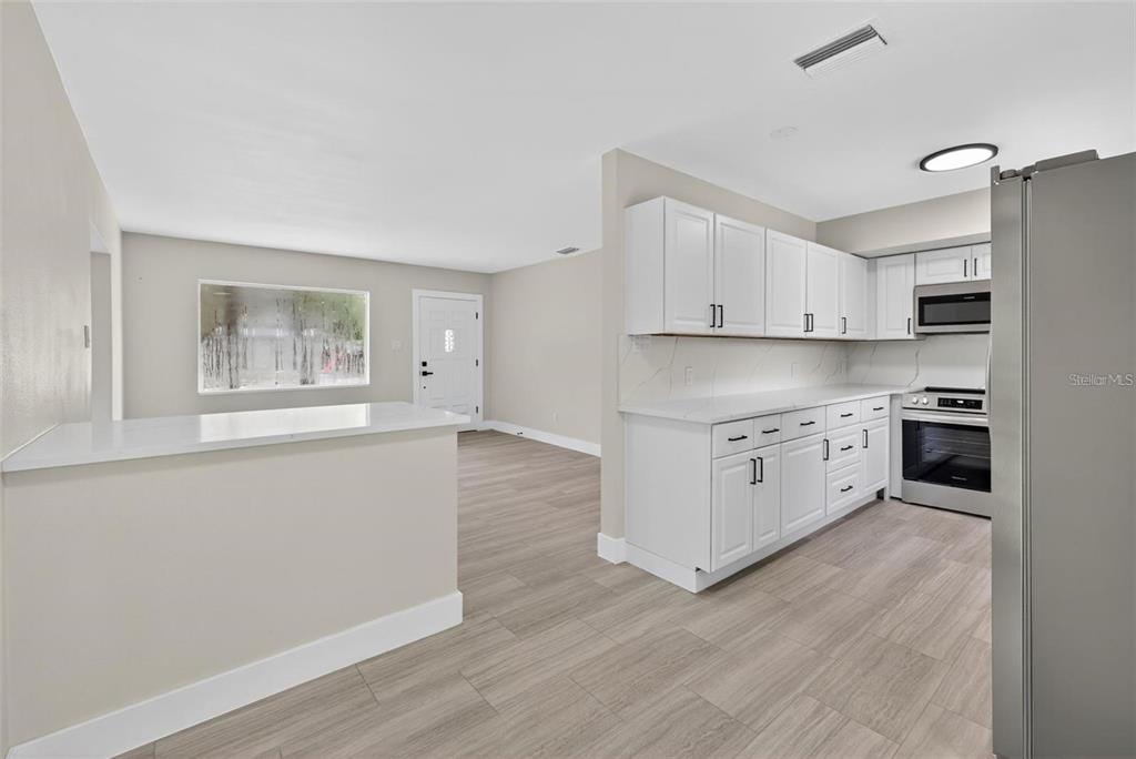 A kitchen with white cabinets, stainless steel appliances, and a peninsula overlooking a living area — 413 COUNTRY CLUB DRIVE, OLDSMAR, FL