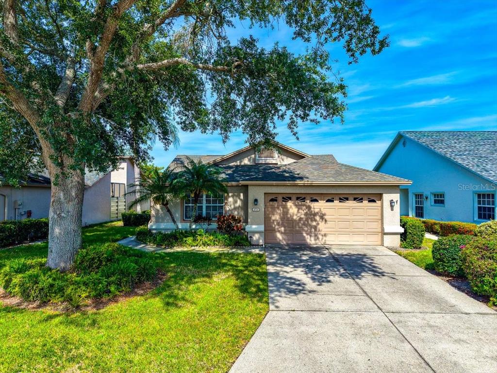 A single-story house with a tan exterior, a two-car garage, and a large front tree — 4734 RAINTREE STREET CIRCLE E, BRADENTON, FL