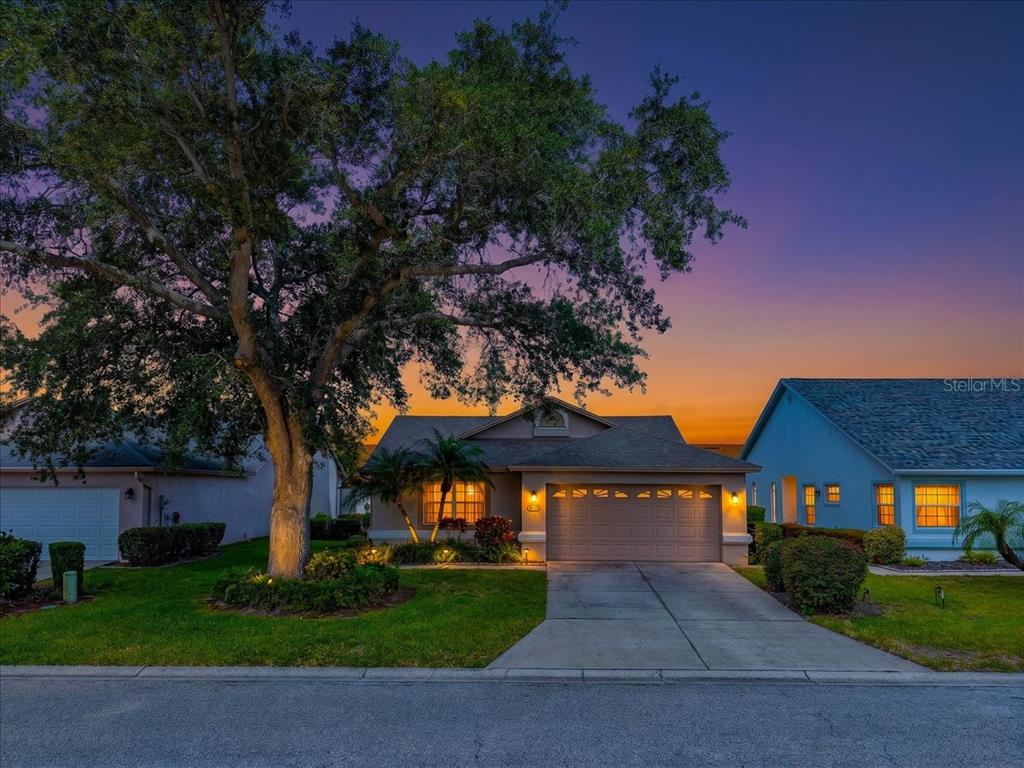 A single-story house with a concrete driveway and a large tree at dusk — 4734 RAINTREE STREET CIRCLE E, BRADENTON, FL