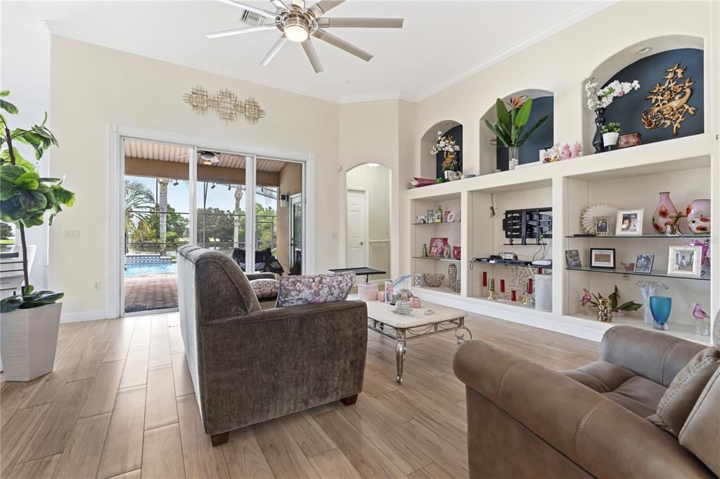 A living room features wood-look tile floors, built-in shelving, and sliding glass doors to a pool — 1605 MARINA LAKE DRIVE, KISSIMMEE, FL