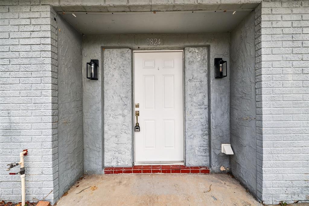 A white front door is centered between two black lanterns on a gray brick exterior — 9824 POCONO STREET, PORT RICHEY, FL