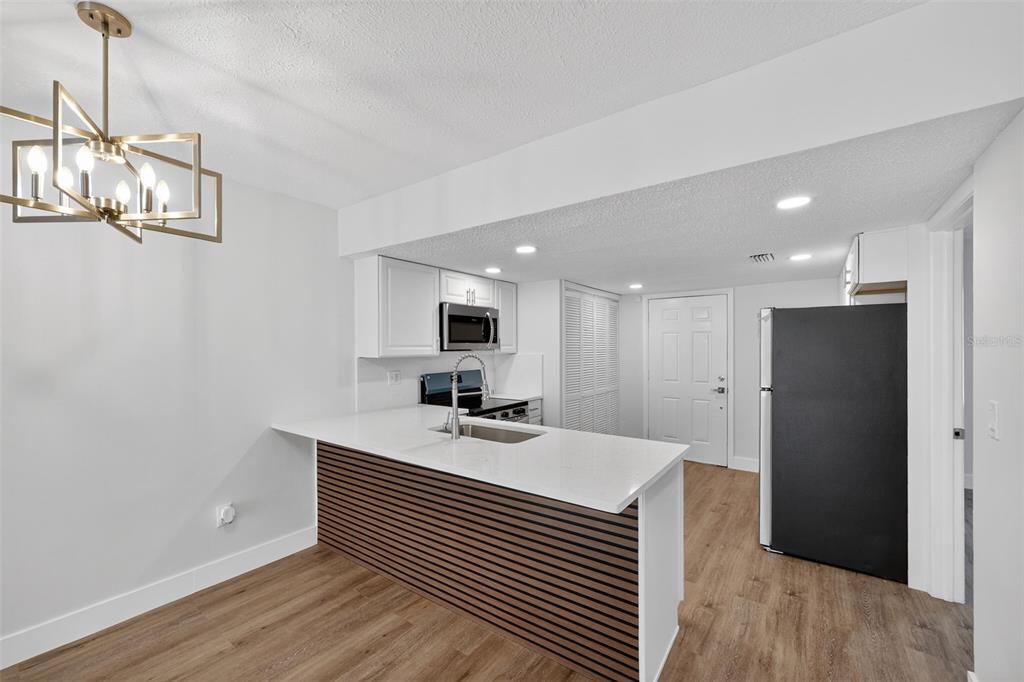 A modern kitchen features white cabinets, a slatted wood island, and a black refrigerator — 9824 POCONO STREET, PORT RICHEY, FL