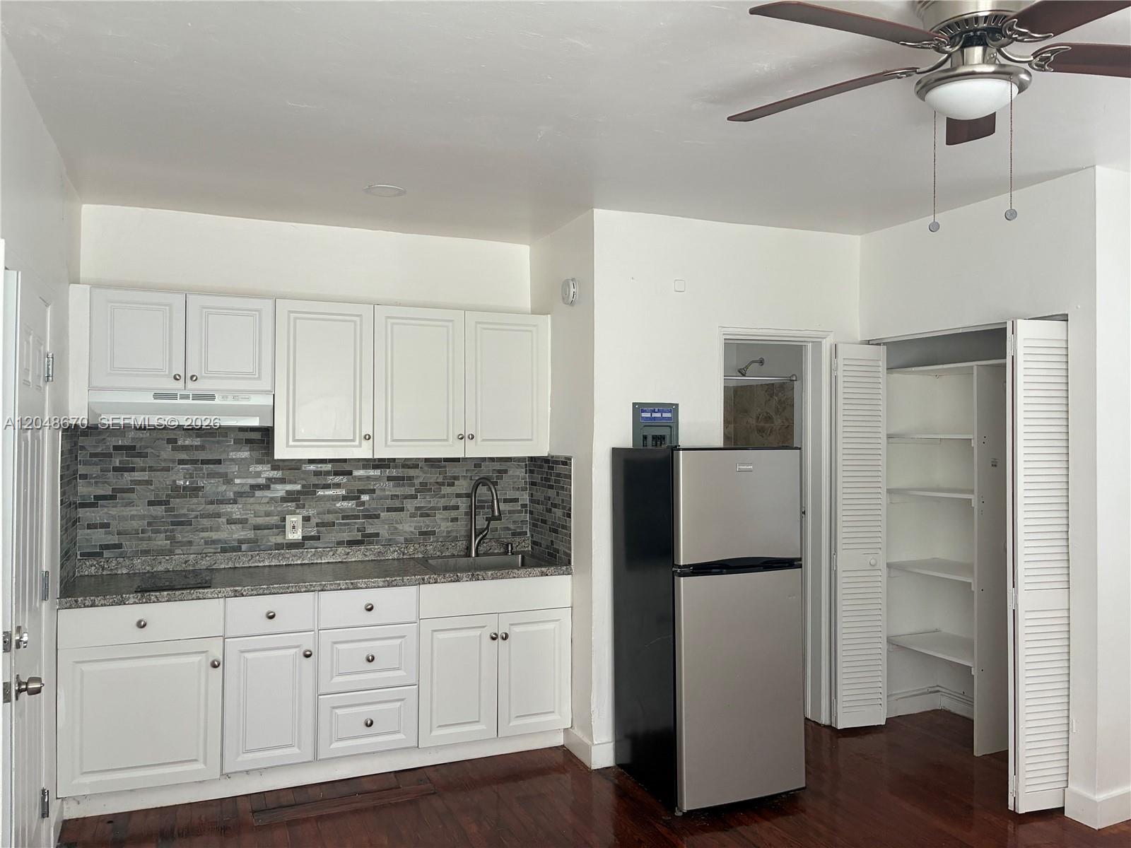 A kitchen features white cabinets, a gray tiled backsplash, stainless steel appliances, and wood flooring — 8020 Abbott Ave # 6, Miami Beach FL 33141, MIAMI BEACH, FL
