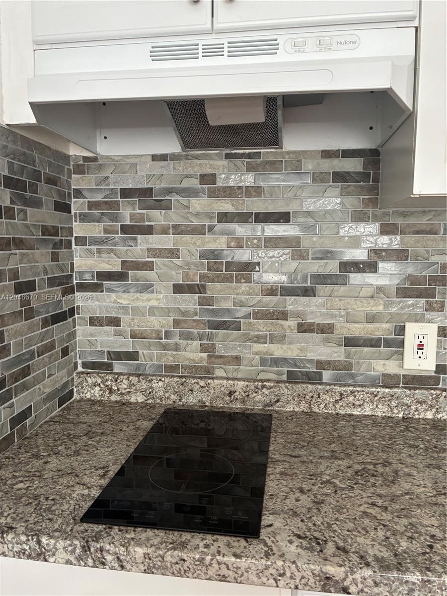 A kitchen features a black electric cooktop, granite countertops, and a multi-toned tile backsplash — 8020 Abbott Ave # 6, Miami Beach FL 33141, MIAMI BEACH, FL