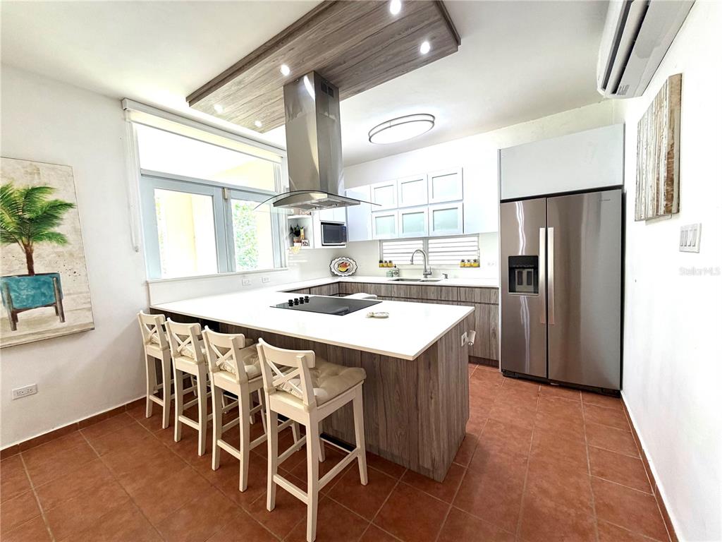 A modern kitchen features a central island with a cooktop, stainless appliances, and wood cabinetry — 693 NORTH COAST VILLAGE UNIT 236, VEGA ALTA, PR