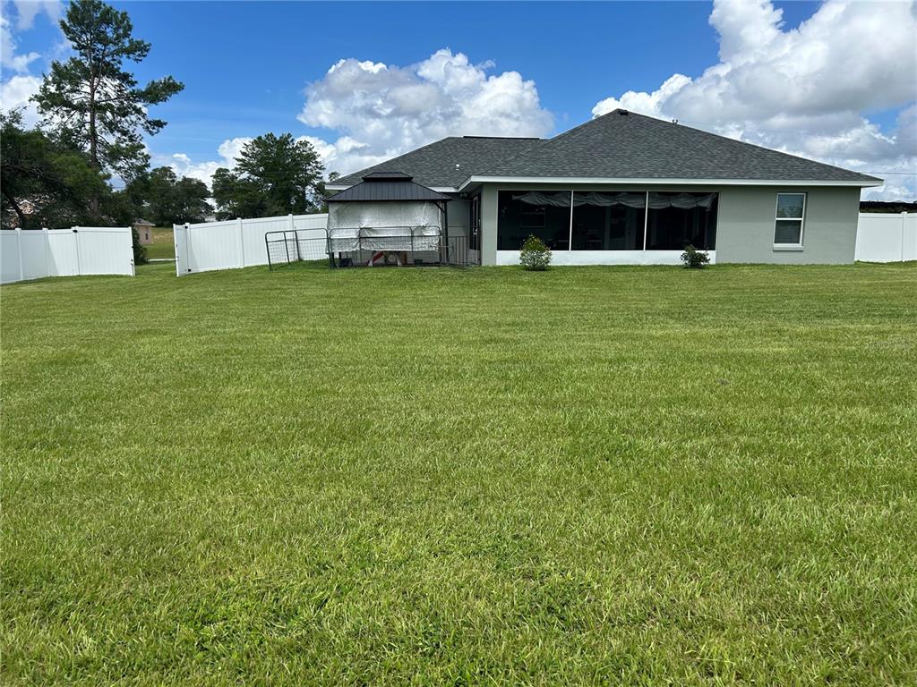 A backyard features a large lawn, a white vinyl fence, and a house with a screened-in patio — 2632 SW 175TH LOOP, OCALA, FL