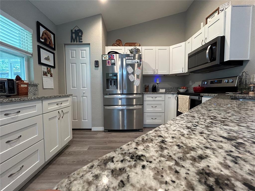 A kitchen features white cabinets, granite countertops, stainless steel appliances, and light wood-look flooring — 2632 SW 175TH LOOP, OCALA, FL