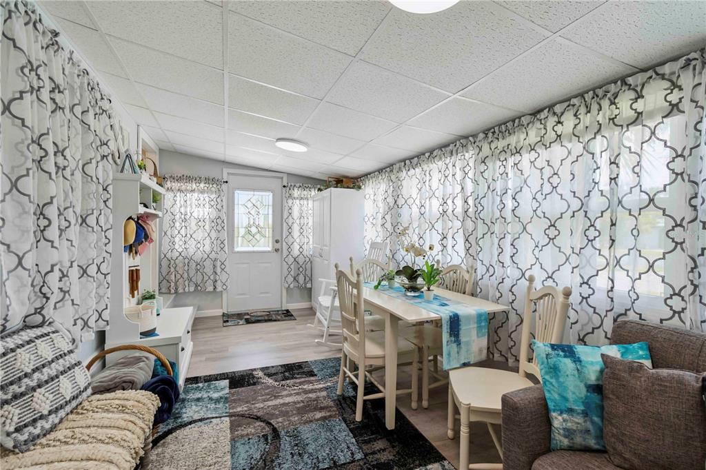 A sunroom features a dining set, patterned curtains, a patterned area rug, and light flooring — 1100 UNIVERSITY PARKWAY UNIT 54, SARASOTA, FL