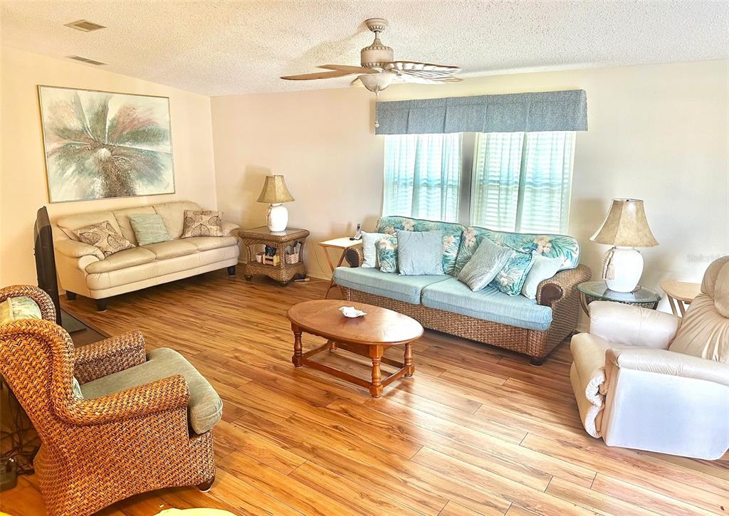 A living room features wood-look flooring, a ceiling fan, and various seating arrangements — 11208 101ST STREET UNIT 115, LARGO, FL
