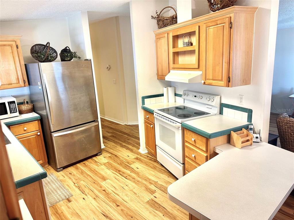 A kitchen with wood cabinets, green-trimmed countertops, stainless steel refrigerator, and wood-look flooring — 11208 101ST STREET UNIT 115, LARGO, FL