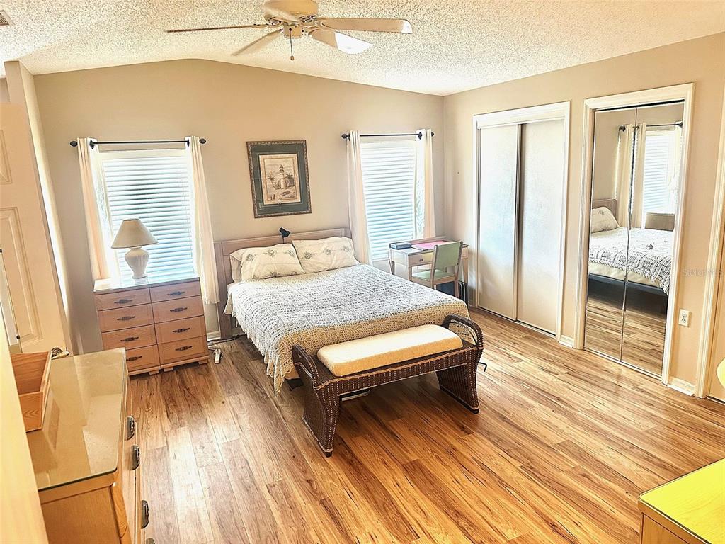A bedroom features a bed, a dresser, a desk, and mirrored closet doors on wood flooring — 11208 101ST STREET UNIT 115, LARGO, FL