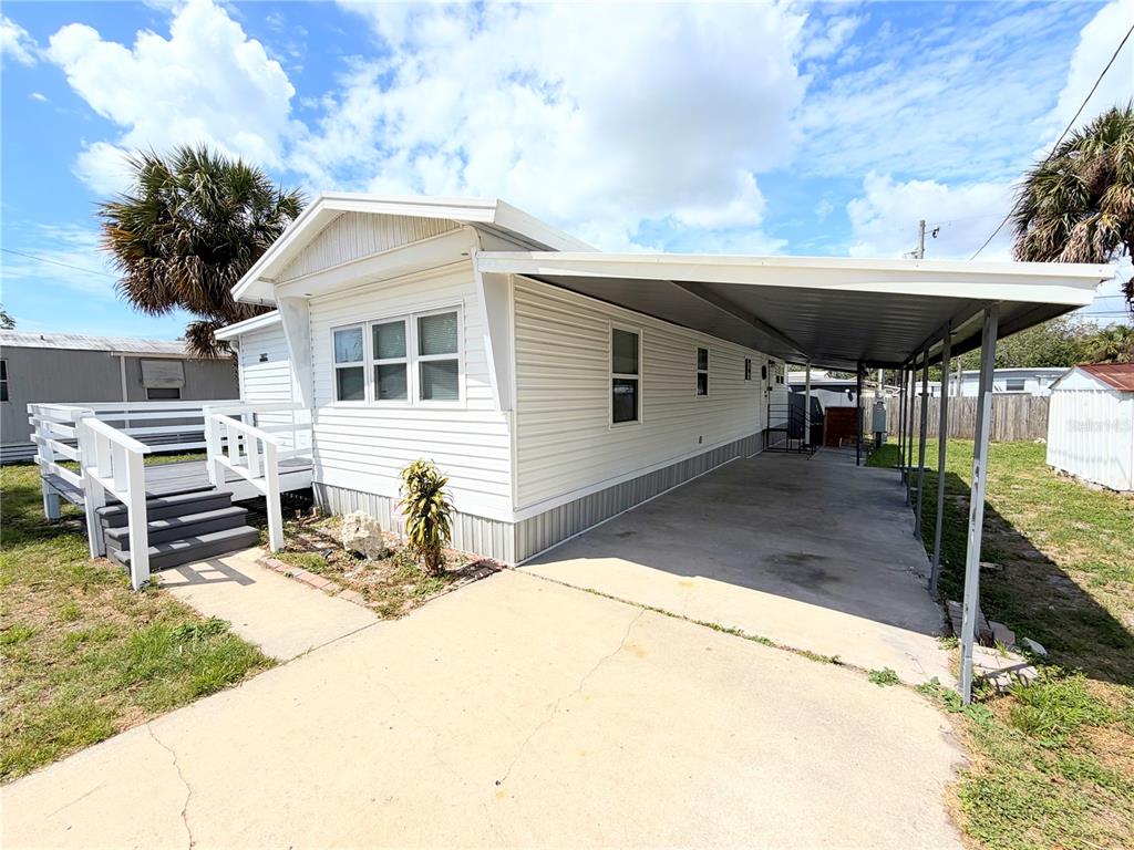 A white mobile home features a side carport, a wooden deck, and a concrete driveway — 7037 LOFTY DRIVE, PORT RICHEY, FL