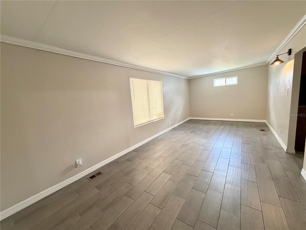 An empty room features light gray walls, a large window, and wood-look tile flooring — 7037 LOFTY DRIVE, PORT RICHEY, FL