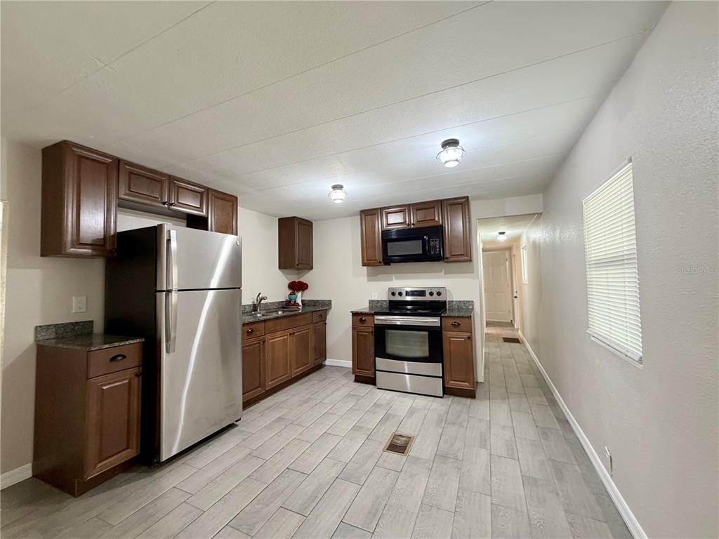 A kitchen features dark wood cabinets, stainless steel appliances, and light gray tile flooring — 7037 LOFTY DRIVE, PORT RICHEY, FL