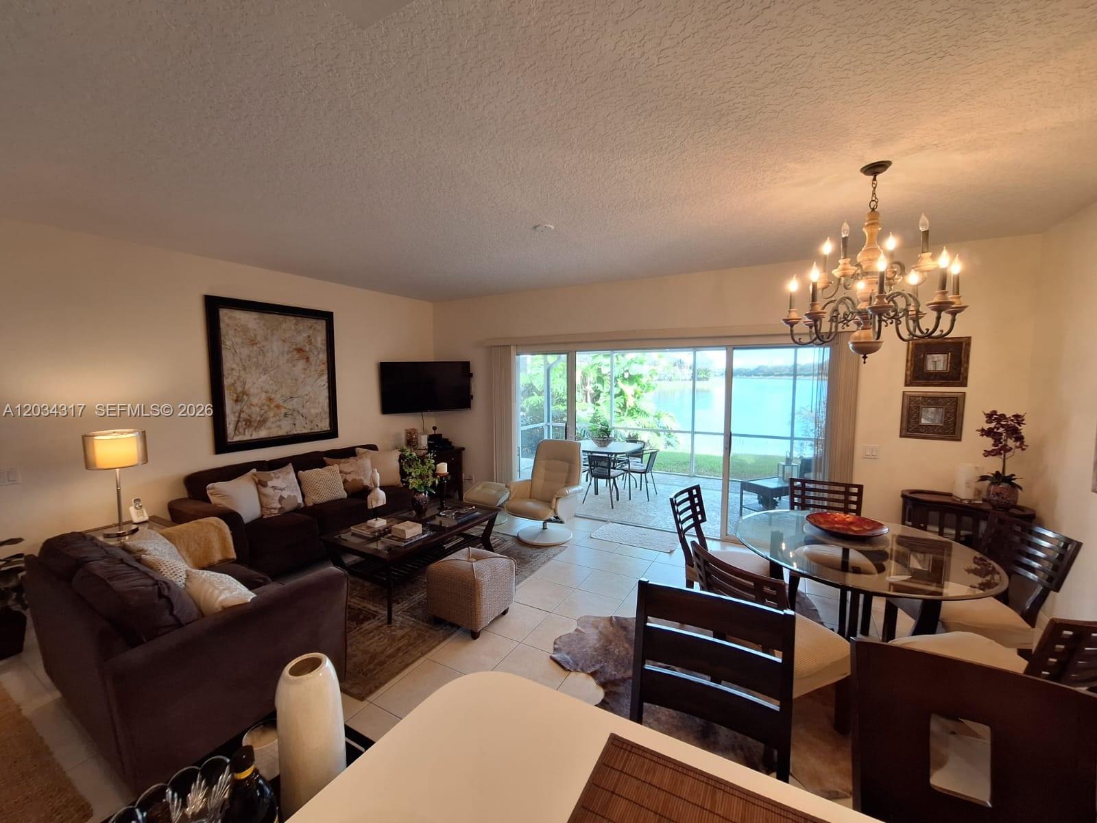 An open-concept living and dining room features tile flooring, a chandelier, and sliding glass doors — 2104 Tigris Dr, West Palm Beach FL 33411, WEST PALM BEACH, FL