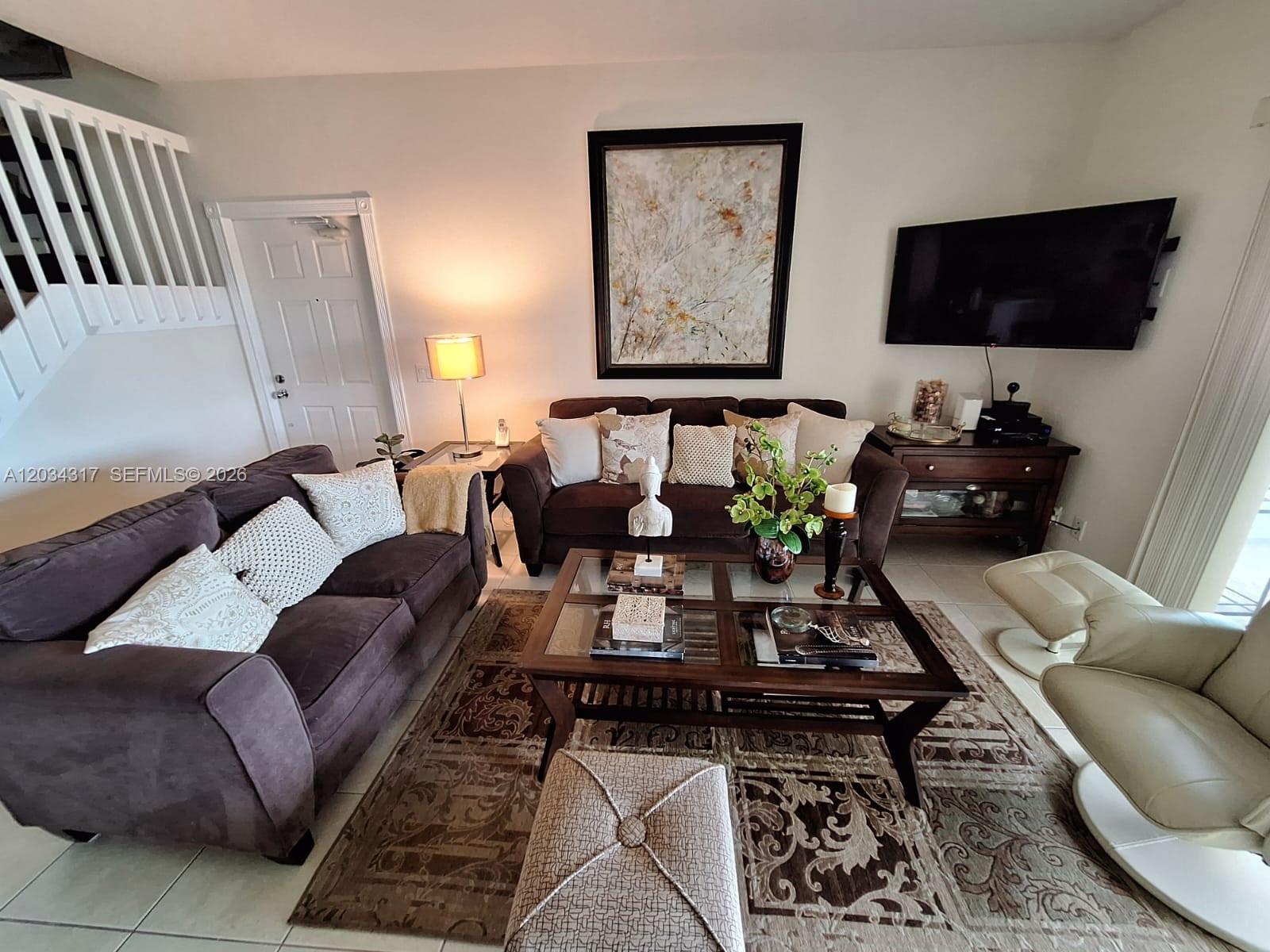 A living room features two brown sofas, a glass-top coffee table, and a wall-mounted television — 2104 Tigris Dr, West Palm Beach FL 33411, WEST PALM BEACH, FL
