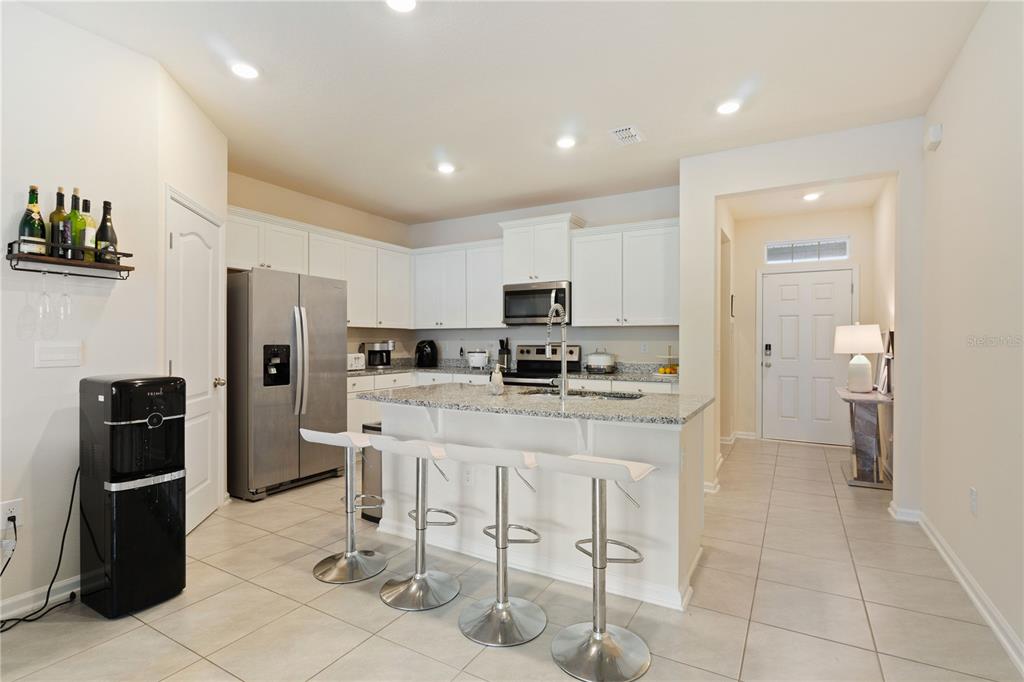 A kitchen features white cabinets, granite countertops, a center island with bar stools, and appliances — 117 REDBUD ROAD, PALM COAST, FL