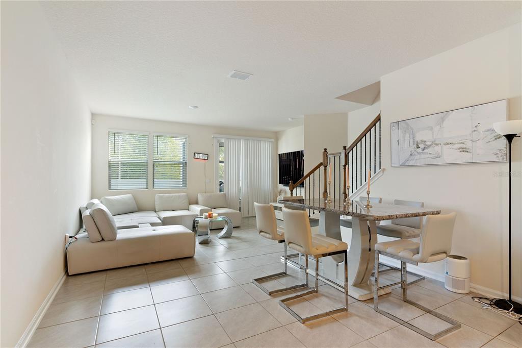 An open-concept living and dining area features light tile flooring, a sectional sofa, and stairs — 117 REDBUD ROAD, PALM COAST, FL