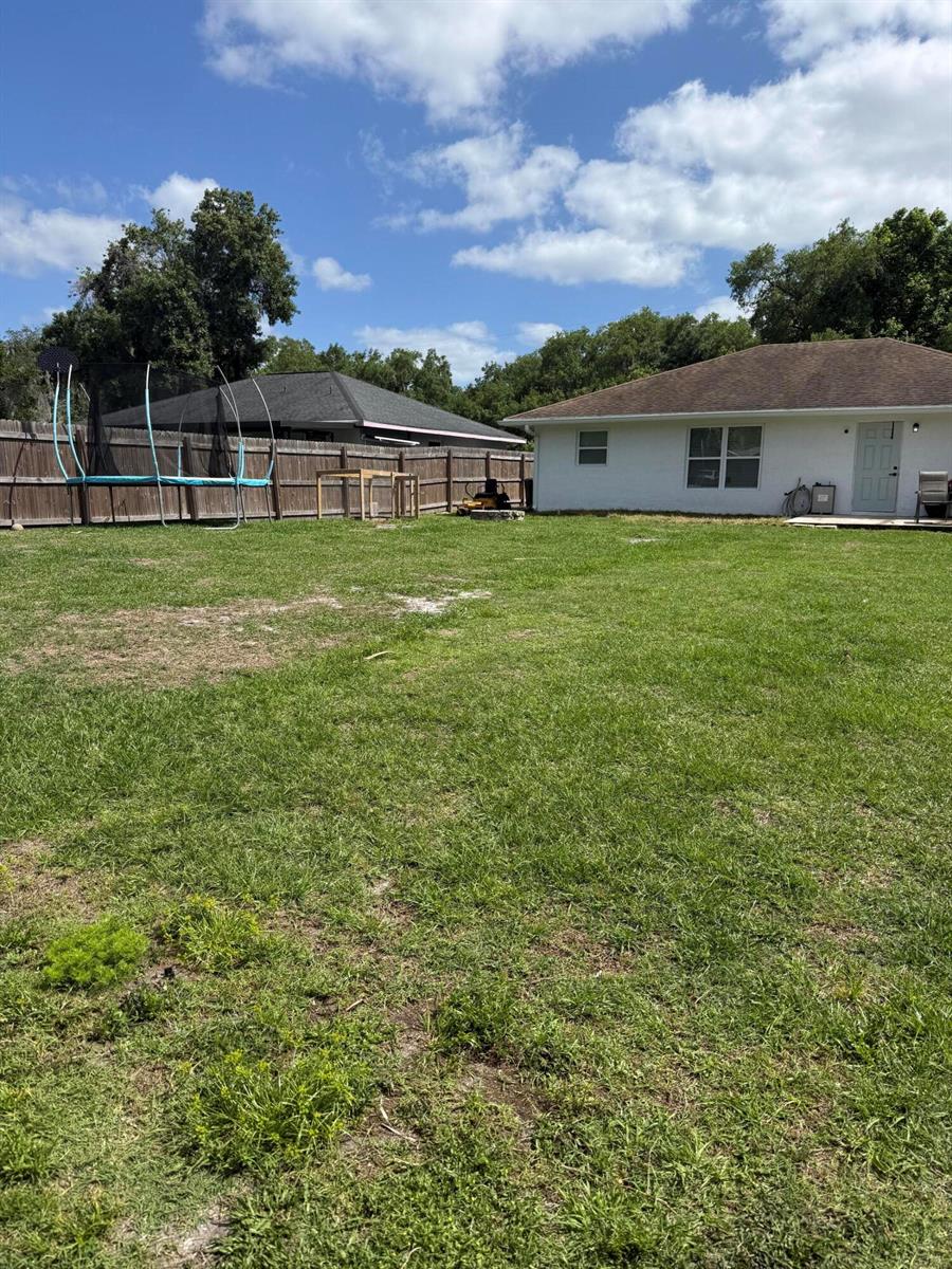A backyard features a trampoline, a wooden fence, and a white house with a roof — 1691 SW 11th Street, Okeechobee FL 34974, OKEECHOBEE, FL