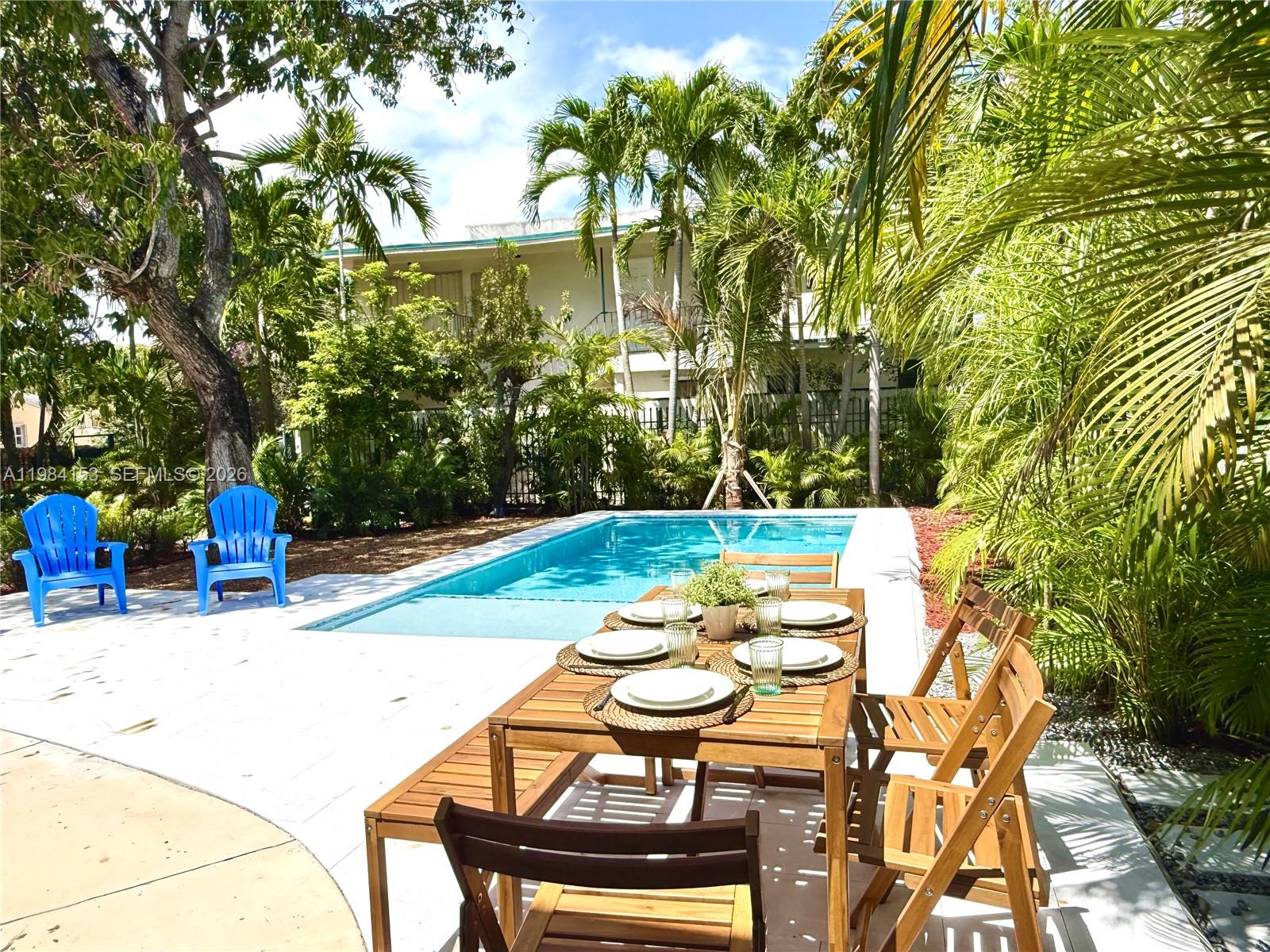 A wooden dining set sits on a patio beside a rectangular swimming pool and palm trees — 1345 SW 14th Ave, Miami FL 33145, MIAMI, FL