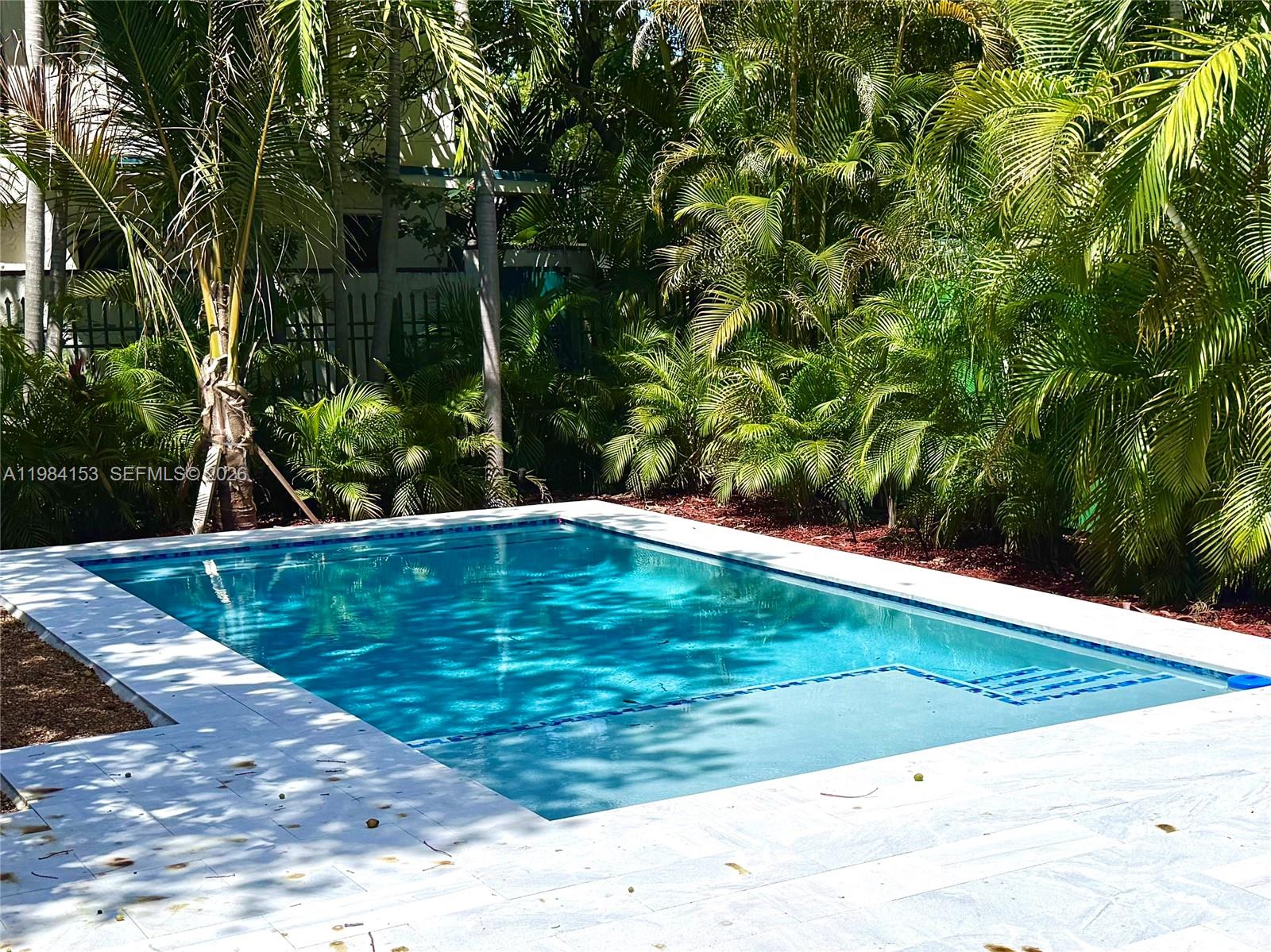 A rectangular swimming pool is surrounded by a light-colored stone deck and lush tropical foliage — 1345 SW 14th Ave, Miami FL 33145, MIAMI, FL