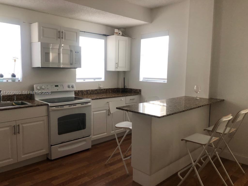A kitchen features white cabinets, granite countertops, a white stove, and a breakfast bar — 737 Jefferson Ave # 103, Miami Beach FL 33139, MIAMI BEACH, FL
