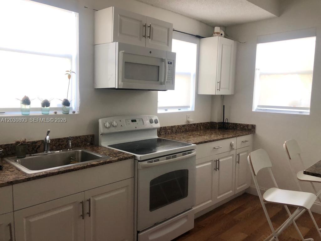 A kitchen features white cabinets, a white stove, a microwave, and brown granite countertops — 737 Jefferson Ave # 103, Miami Beach FL 33139, MIAMI BEACH, FL