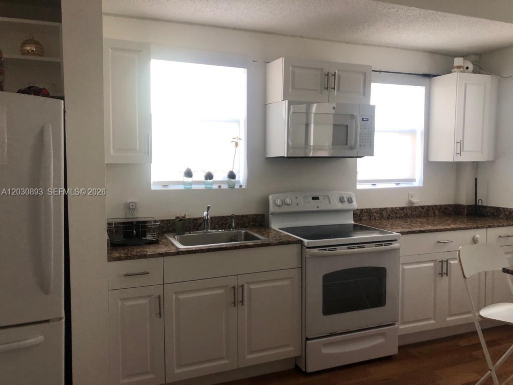 A kitchen features white cabinets, granite countertops, a white stove, and a microwave — 737 Jefferson Ave # 103, Miami Beach FL 33139, MIAMI BEACH, FL
