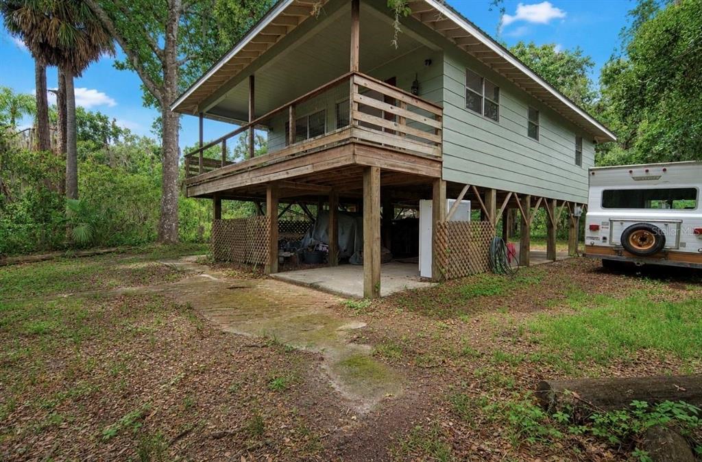 An elevated house with a wooden deck and lattice skirting stands in a wooded lot — 707 GEORGE STREET S, TARPON SPRINGS, FL
