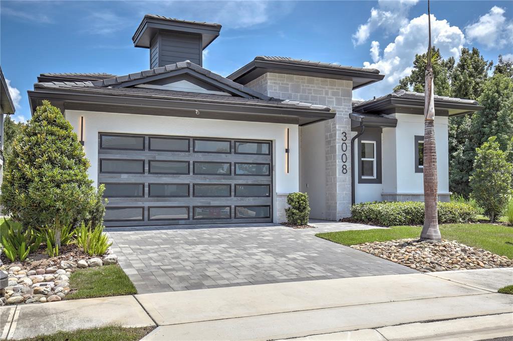 A modern single-story house features a multi-paneled garage door, stone accents, and a paved driveway — 3008 KENSINGTON AVENUE, DAVENPORT, FL