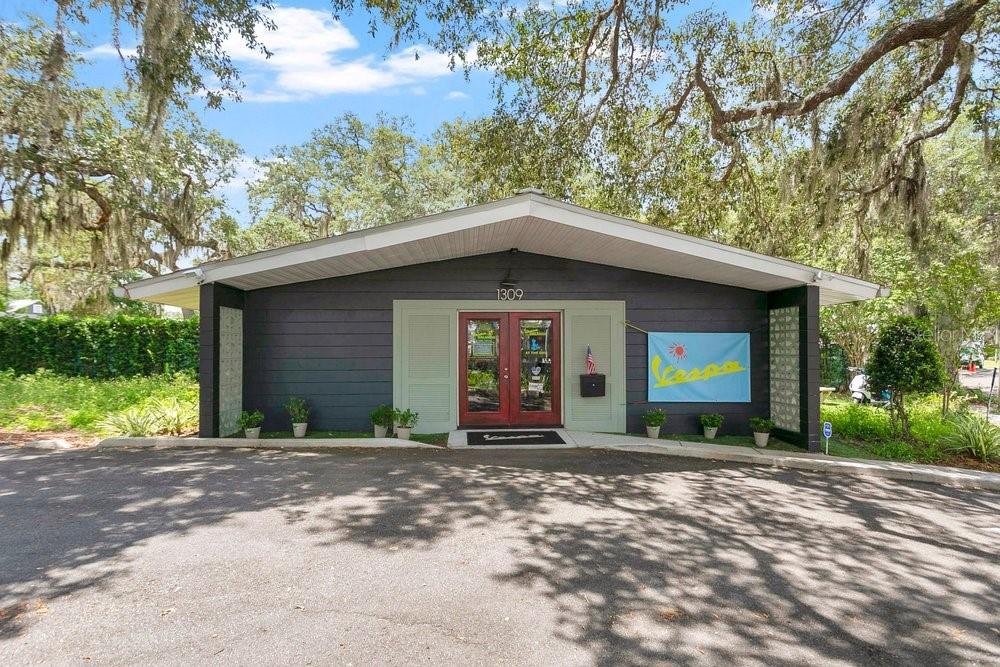 The exterior of a single-story building features dark horizontal siding, red double doors, and landscaping — 1309 WILFRED DRIVE, ORLANDO, FL