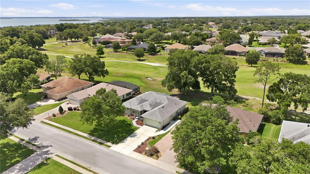 An aerial view shows a suburban neighborhood with houses, green lawns, and a golf course — 5453 GROVE MANOR, LADY LAKE, FL