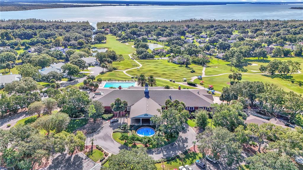 An aerial view shows a clubhouse with a pool and fountain surrounded by a golf course — 5453 GROVE MANOR, LADY LAKE, FL