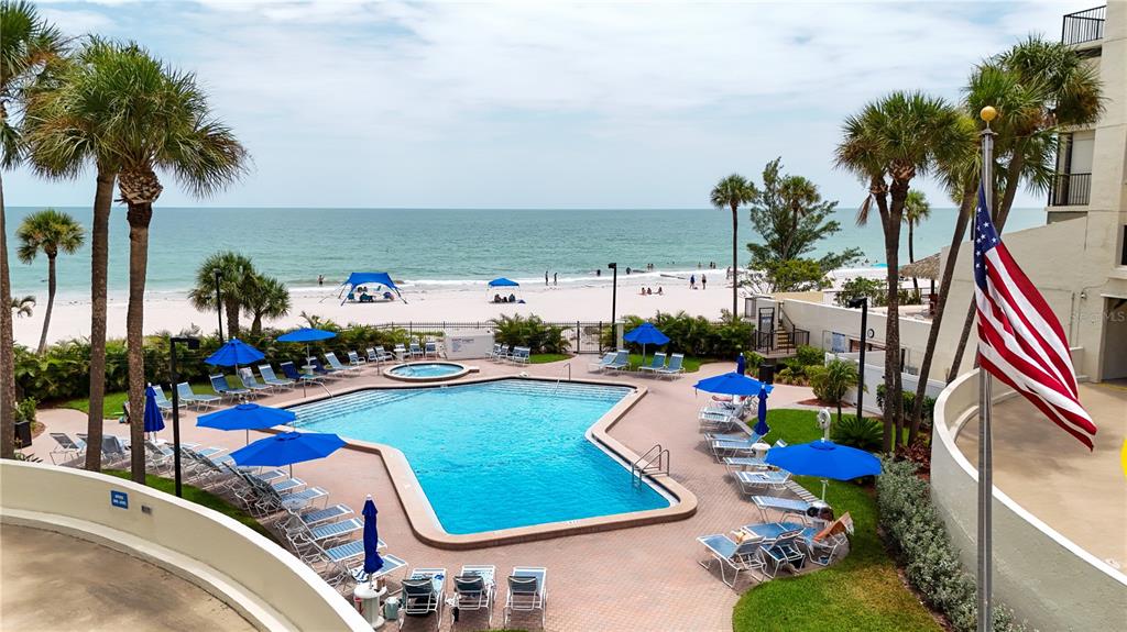 An elevated view of a swimming pool and patio area overlooking a sandy beach — 15000 GULF BOULEVARD UNIT 907, MADEIRA BEACH, FL