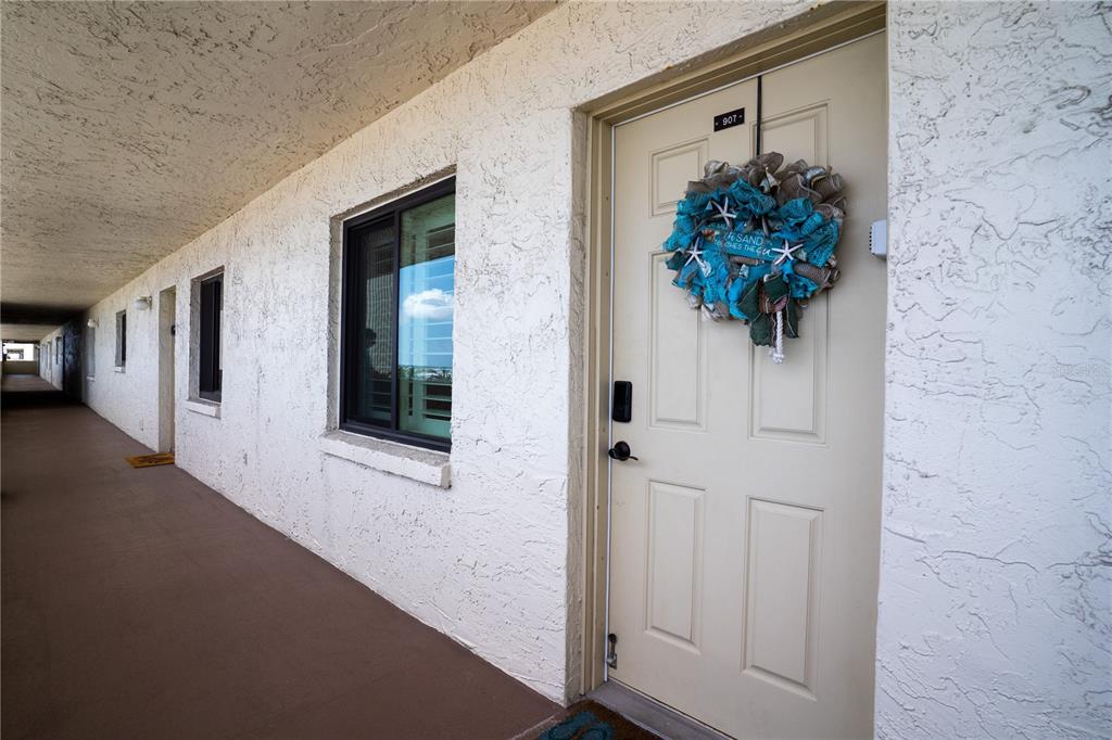 A beige door with a decorative wreath sits along an outdoor apartment building walkway — 15000 GULF BOULEVARD UNIT 907, MADEIRA BEACH, FL