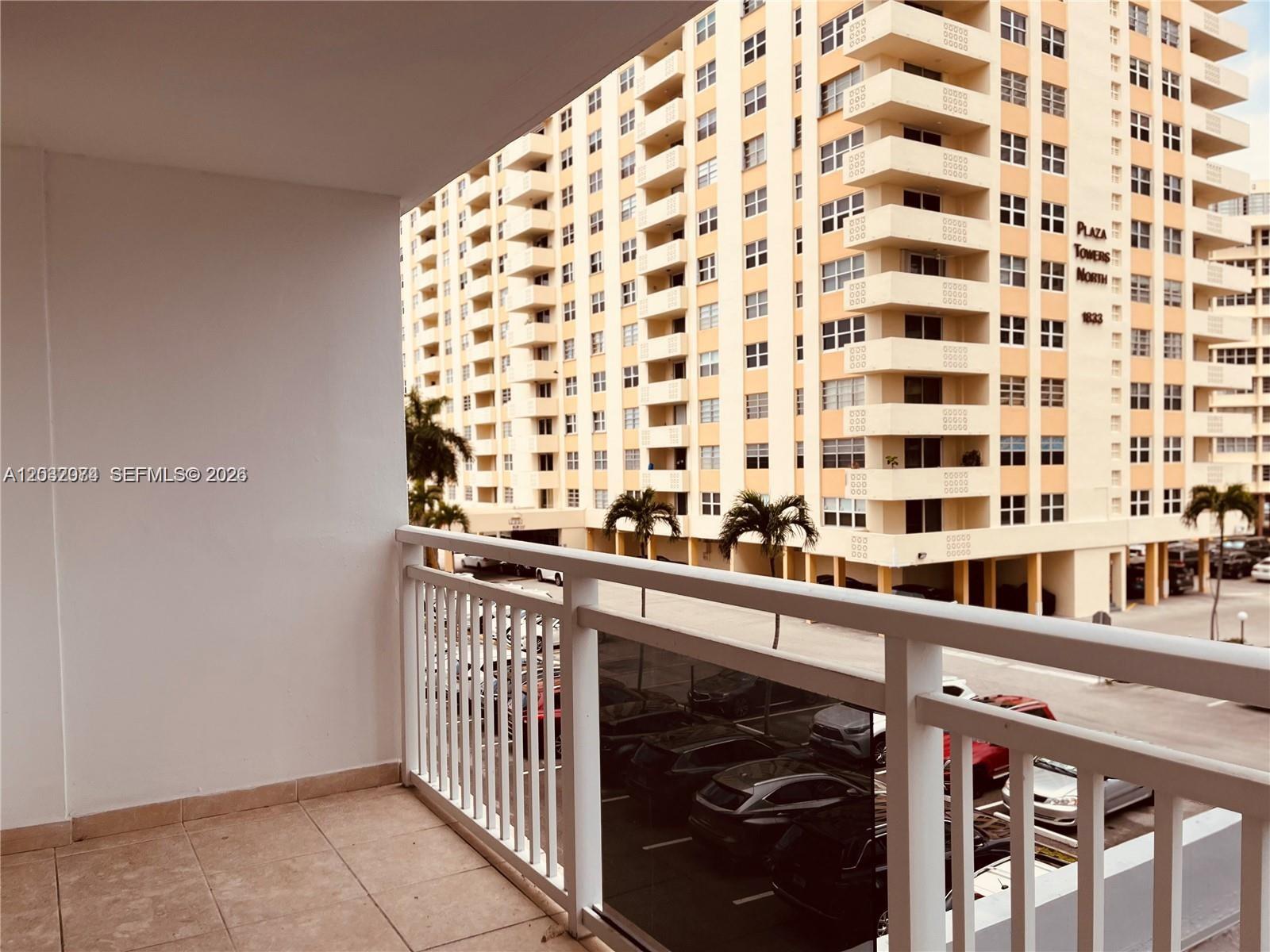 A balcony with tiled flooring and a white railing overlooks a parking lot and building — 1849 S Ocean Dr # 0, Hallandale Beach FL 33009, HALLANDALE BEACH, FL