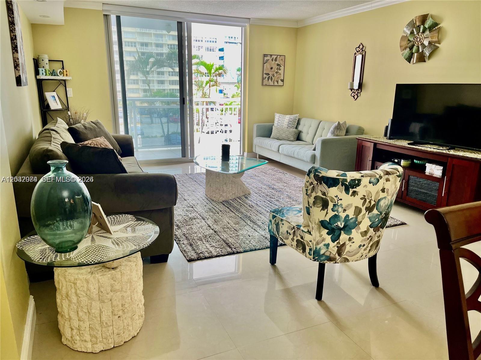 A living room features a sofa, floral armchair, glass coffee table, and a balcony view — 1849 S Ocean Dr # 0, Hallandale Beach FL 33009, HALLANDALE BEACH, FL