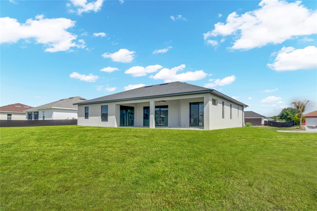 The exterior rear view of a single-story house features a covered patio and lawn — 2915 23RD STREET SW, LEHIGH ACRES, FL