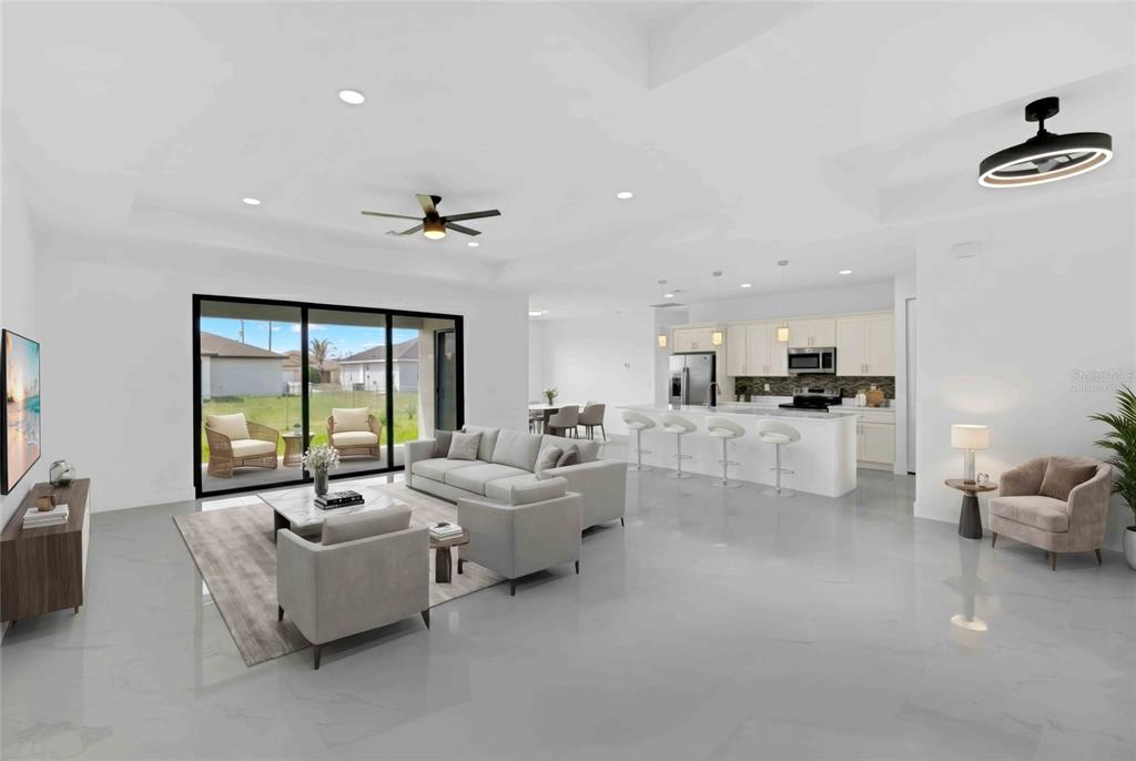 A bright open-concept living room and kitchen featuring white tile floors and sliding glass doors — 2915 23RD STREET SW, LEHIGH ACRES, FL